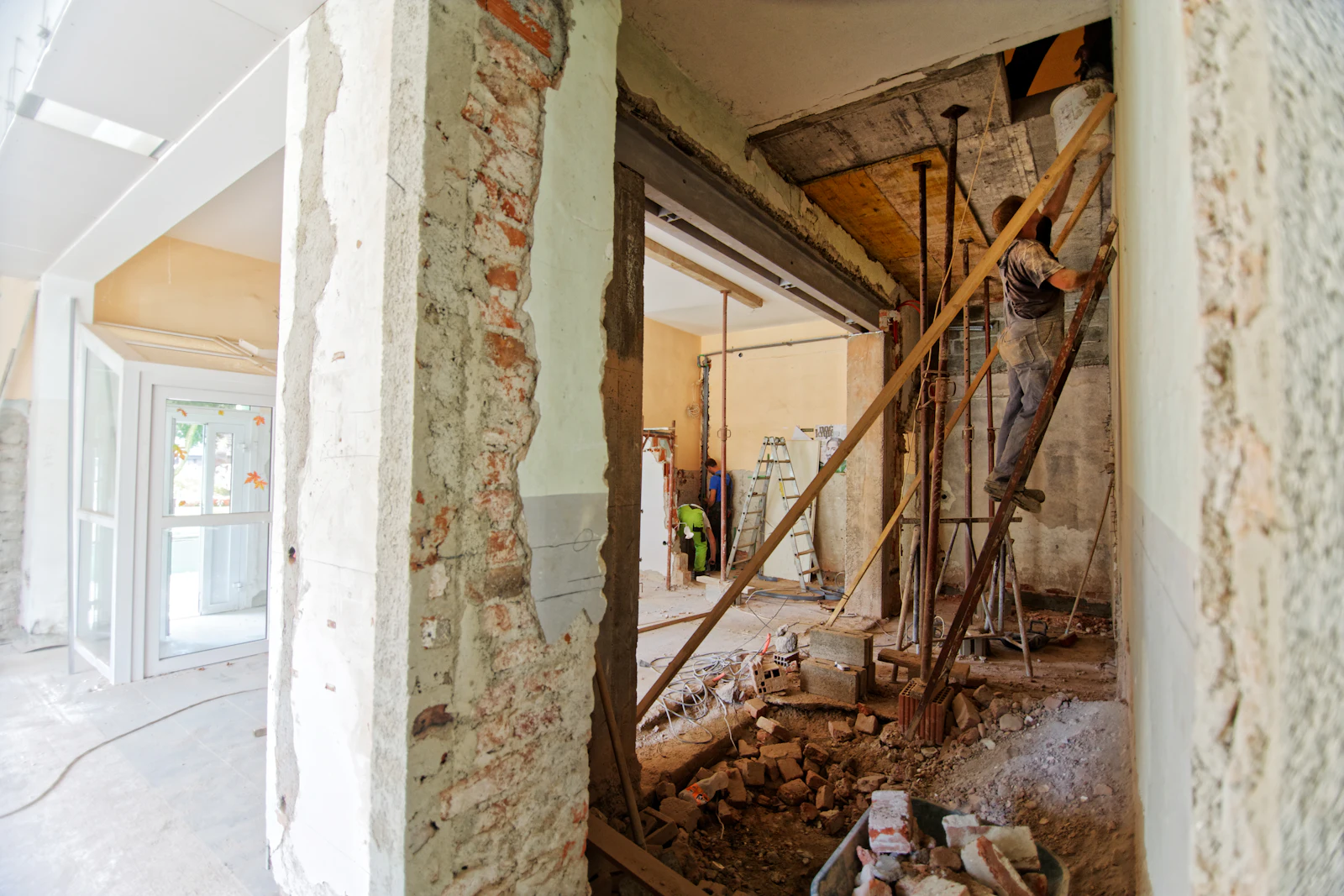 A worker on a ladder rebuilding a room, with bare brick and new walls going in