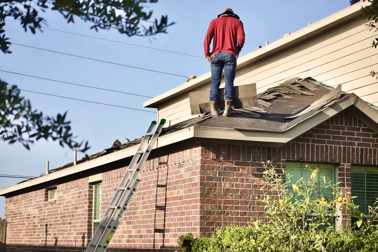A roofer tearing off old shingles on a brick house before the new roof goes on