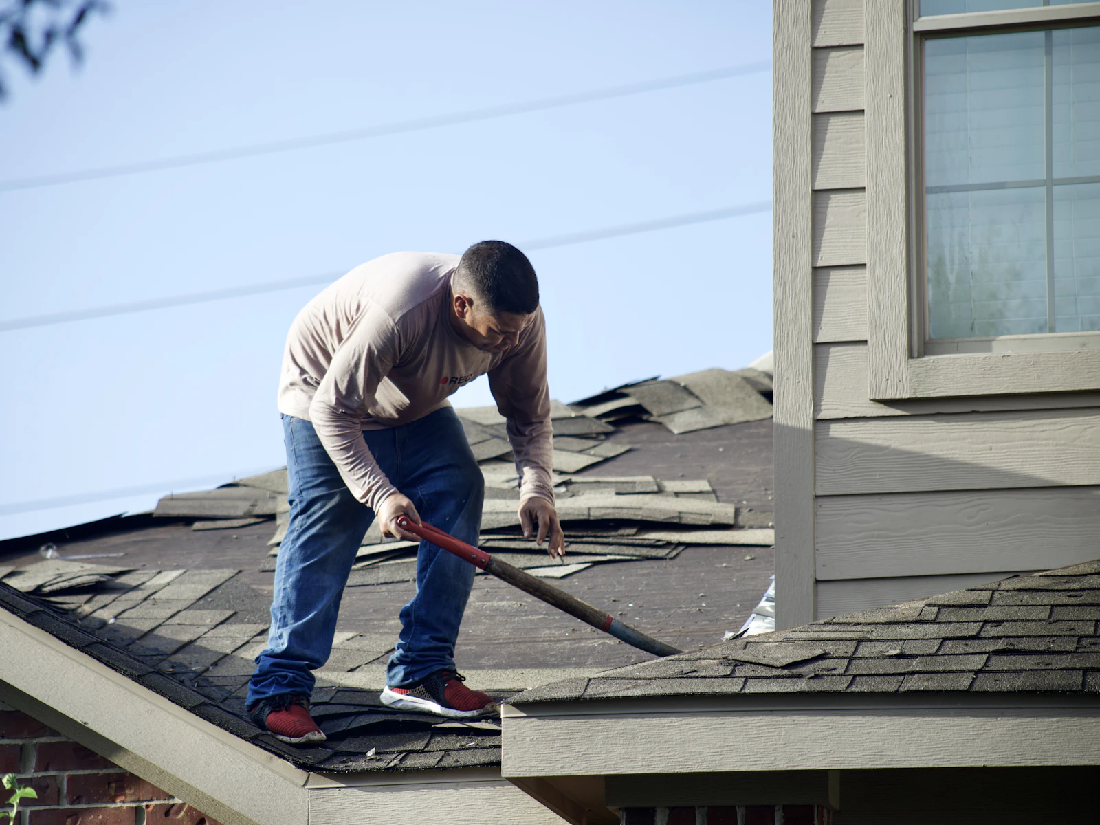 A roofer removing old shingles from a house roof
