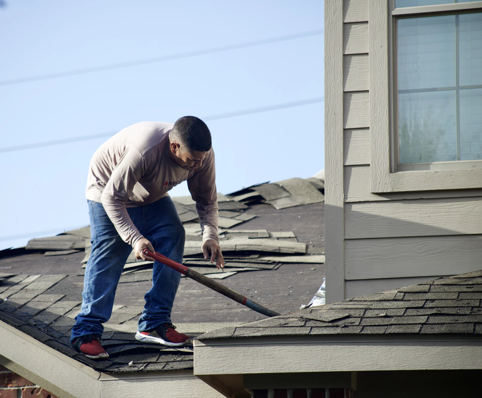 A roofer removing old shingles from a house roof