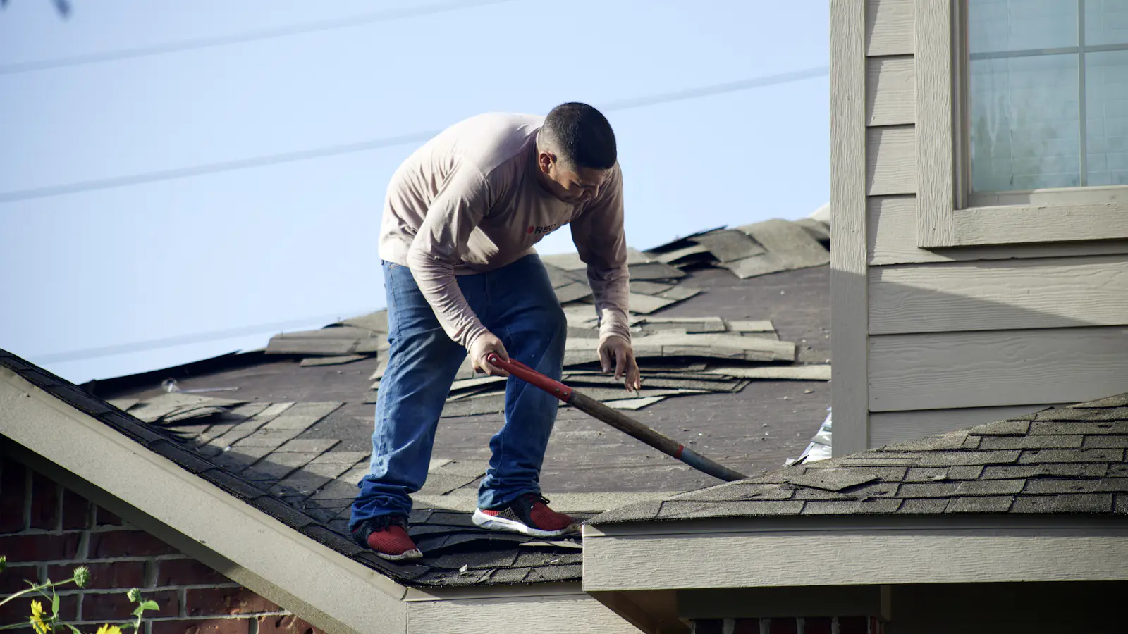 A roofer removing old shingles from a house roof