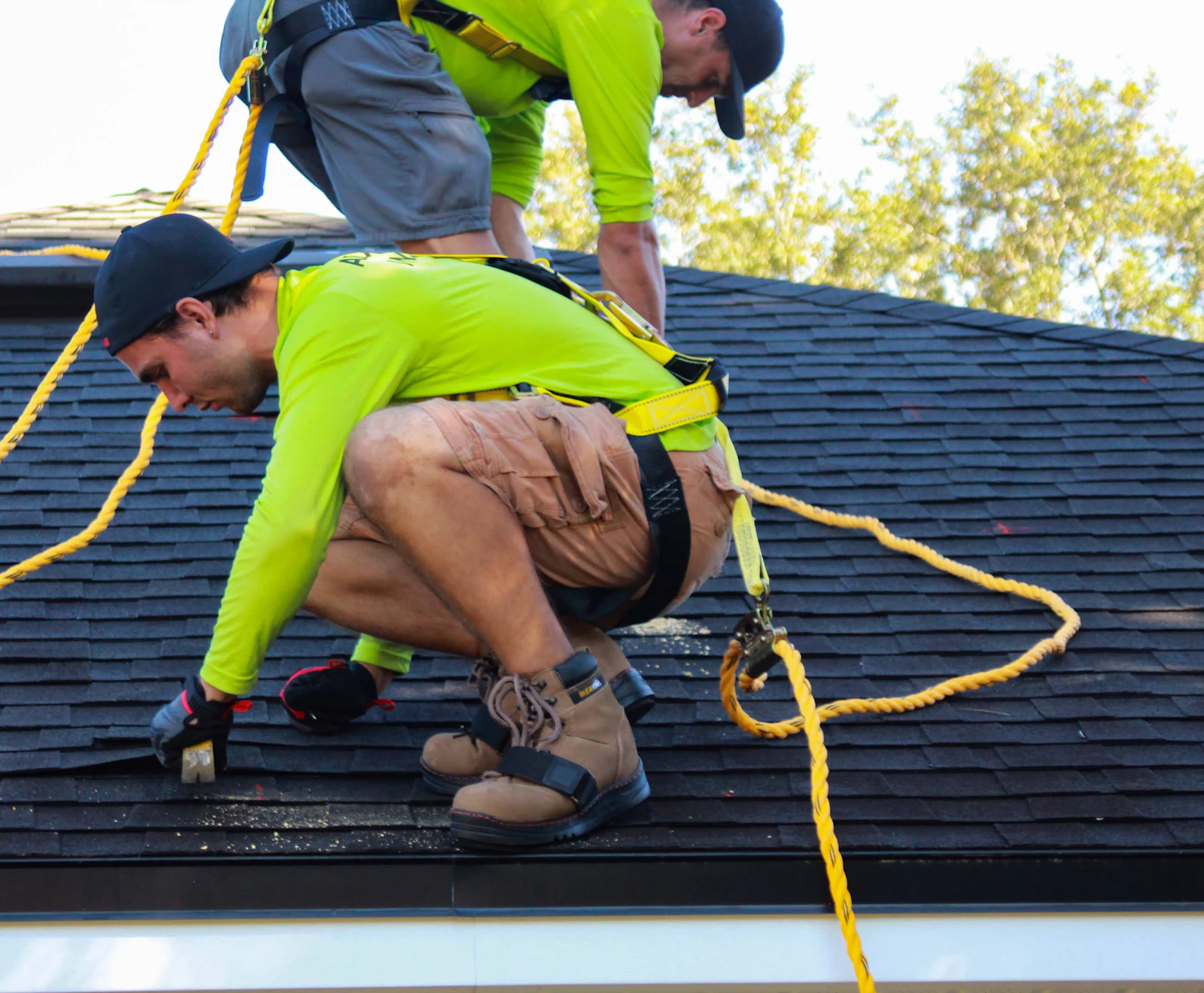 A roofer in a safety harness checking a shingle roof