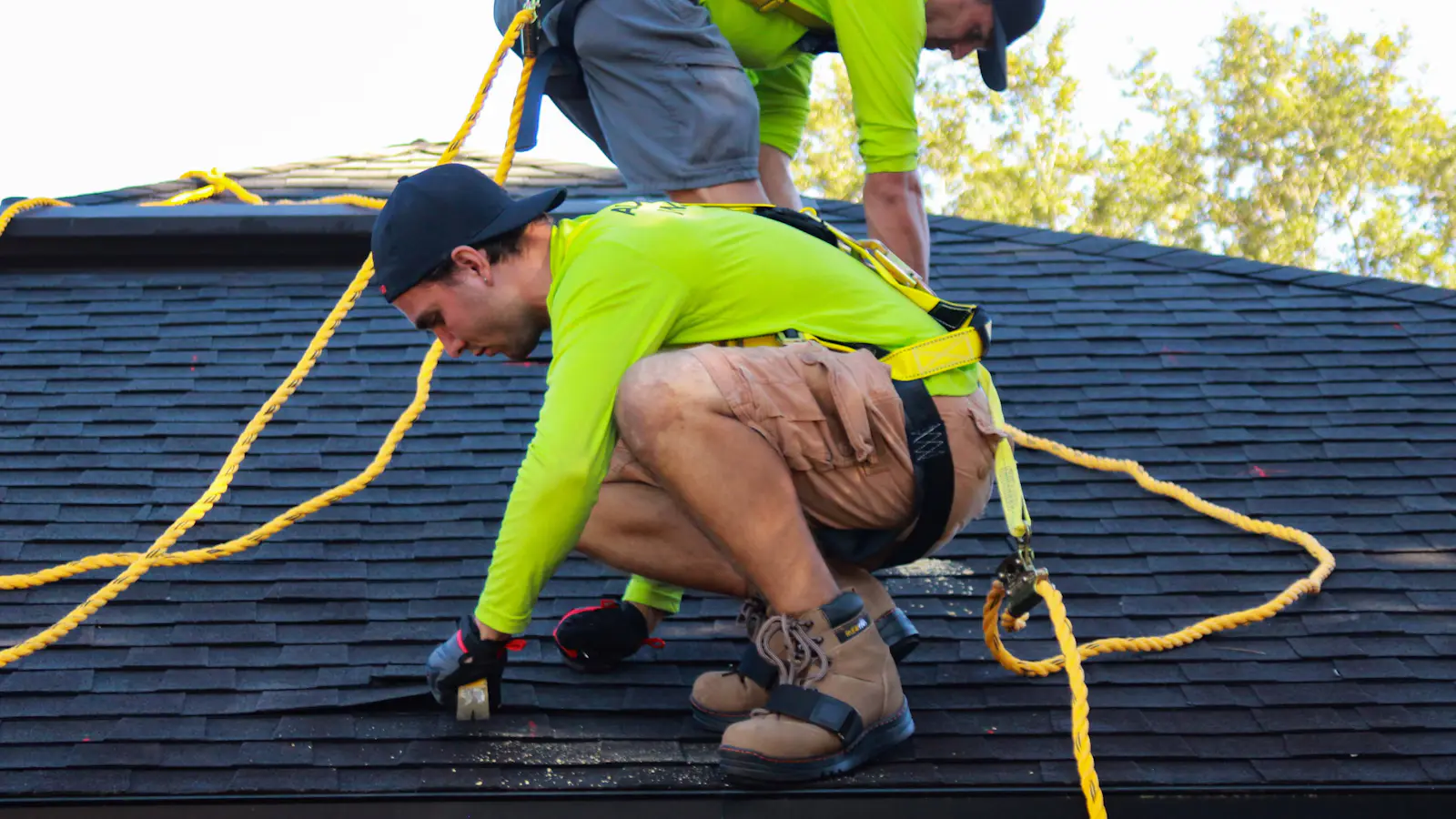 A roofer in a safety harness checking a shingle roof