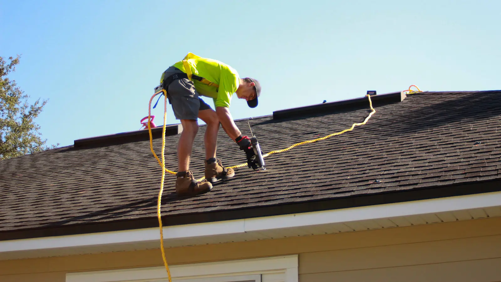 A roofer fixing a shingle roof with a drill