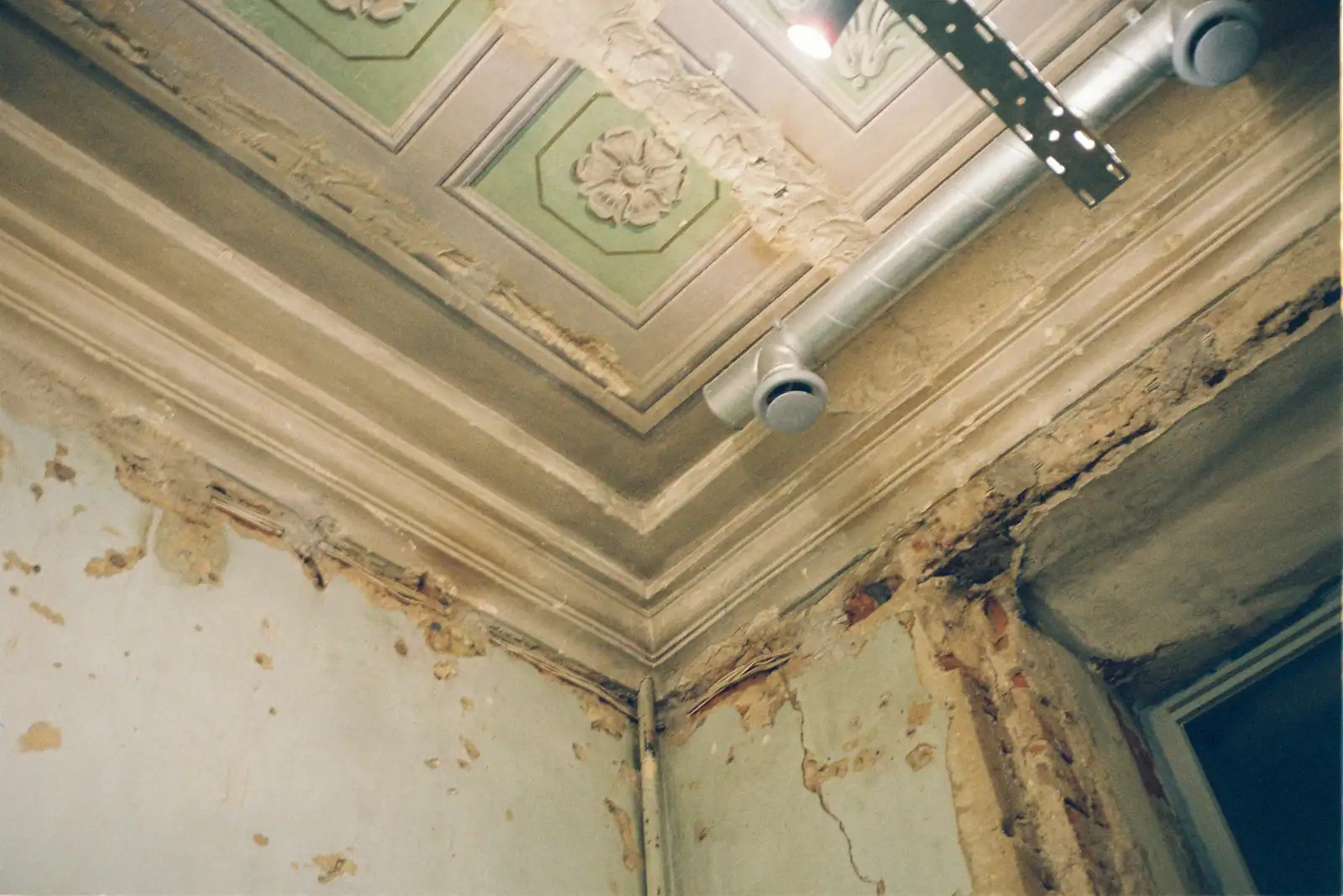 A vintage ceiling and wall corner with water damage, crumbling plaster and peeling paint