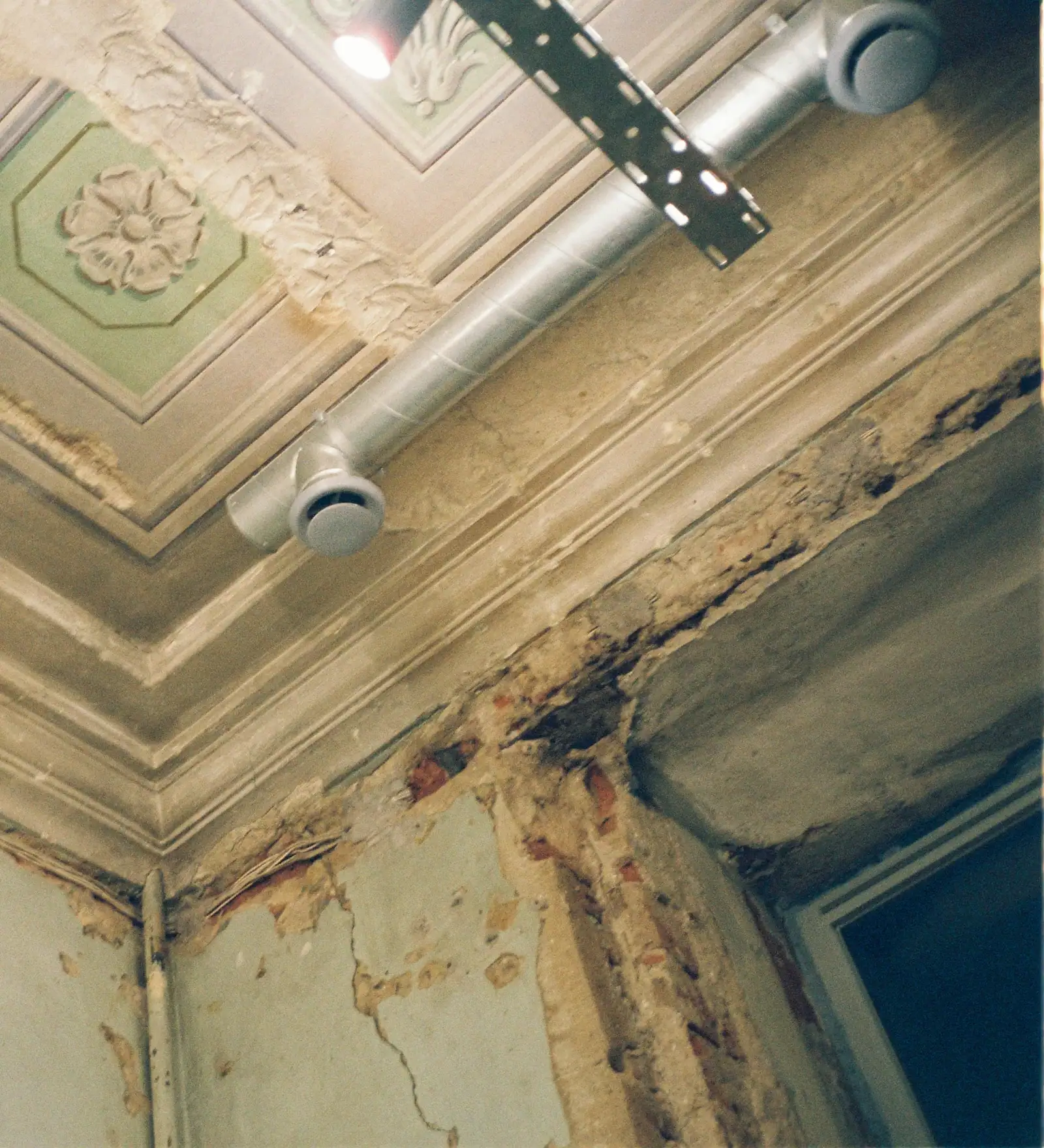 A vintage ceiling and wall corner with water damage, crumbling plaster and peeling paint