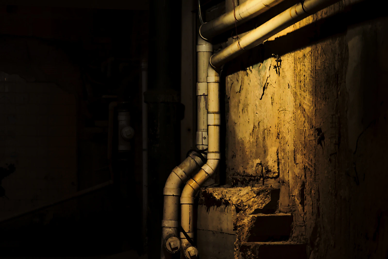 Old pipes running down a damp basement wall