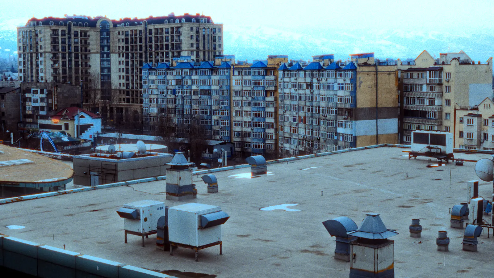 A flat roof with vents, looking across to apartment buildings